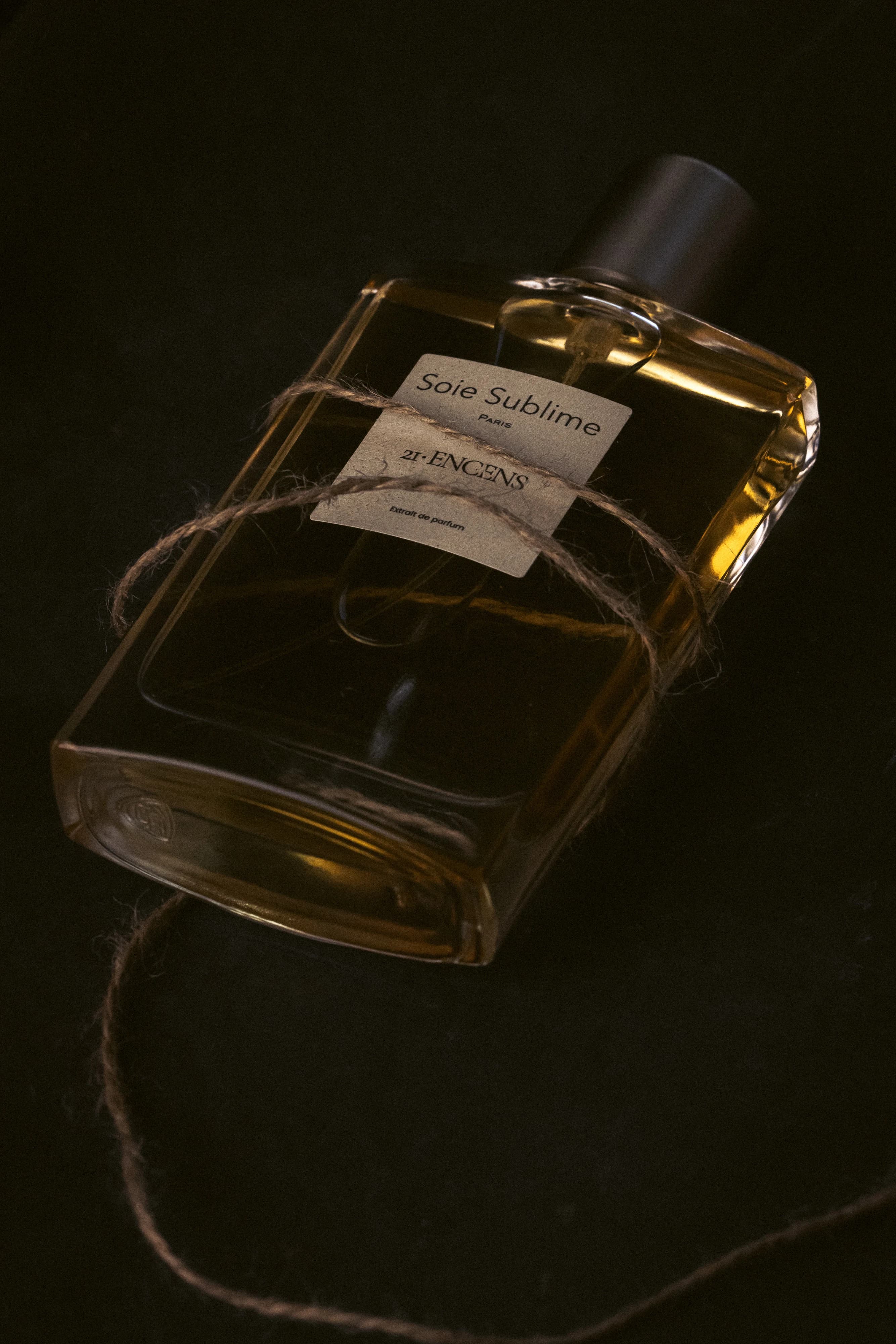 ENCENS bottle on a black surface, wrapped in jute cord under warm low light